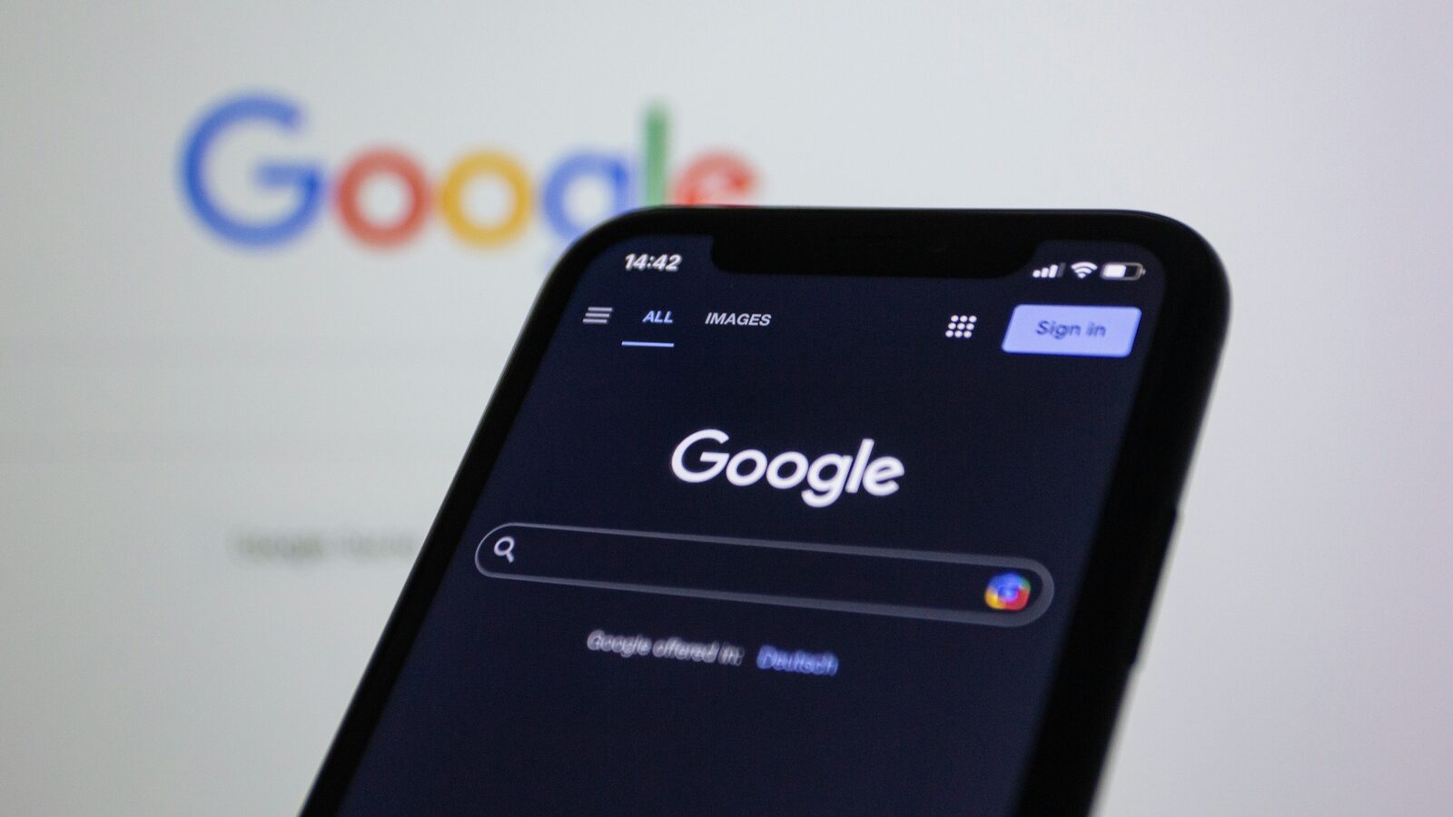 Un smartphone affichant la recherche Google devant un écran d’ordinateur